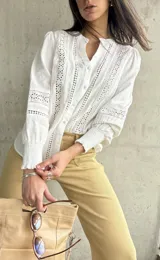 Camisa blanca de manga larga con detalles de broderie y calados en el frente y las mangas. Tiene cuello mao y cierre frontal con botones. Los puños son elásticos.