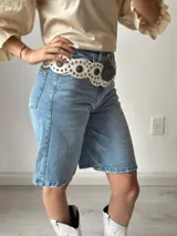 Bermuda de jean celeste de corte ancho, con cintura alta y largo a la rodilla. Presenta ruedo desflecado y se complementa con un cinturón ancho de cuero negro con tachas plateadas.