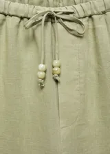 Pantalón color crudo de lino, corte recto, tiro medio, con cintura elástica ajustable con lazo, bolsillos laterales y traseros.