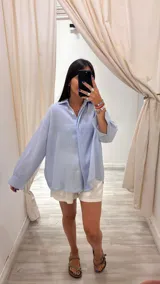 Camisa color beige claro con textura brillante, cuello clásico, cierre frontal con botones y mangas largas con puños abotonados.