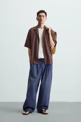 Camisa de manga corta con cuello bowling y calce relajado. Presenta un tejido con textura estructurada y efecto lavado, con cierre frontal de botones al tono.