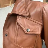 Campera marrón de cuero ovino con cuello clásico, cierre frontal con botones a presión, bolsillos con solapa en el pecho y mangas largas con puños abotonados.