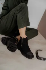 Bota corta negra de cuero sintético, con punta cuadrada, cierre lateral con cremallera y suela track. Incluye correa desmontable con apliques metálicos.