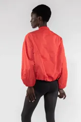 Campera bomber color beige, corte regular, con cierre frontal con cremallera visible, cuello acanalado, puños y bajo elásticos fruncidos, hombro caído, bolsillos de ribete verticales y bolsillo utilitario con cremallera en la manga.