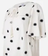 Vestido corto evasé color crema con estampado de soles negros, cuello redondo con lazo, mangas cortas y bajo con volantes.