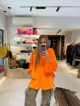 Buzo tipo canguro oversize de tela plush, color azul claro. Presenta capucha, cierre frontal parcial con cordón turquesa y bolsillos canguro frontales. Las mangas son largas y abullonadas con puños ajustados.