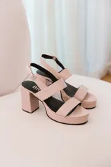 Sandalias de tacón color rosa nude, con plataforma delantera y dos tiras anchas sobre el empeine. Presentan una tira delgada con hebilla alrededor del tobillo y un tacón cuadrado.