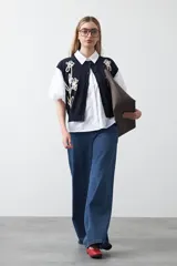 Chaleco de punto color blanco con bordado aplicado de cordón marrón en diseño floral. Presenta cierre frontal de botones al tono, cuello redondo y terminaciones acanaladas en sisas y ruedo.