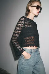 Jersey corto de punto calado negro, con cuello redondo amplio y mangas largas acampanadas.