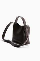 Cartera bandolera de cuero sintético color marrón oscuro, con asa corta superior y correa larga ajustable. Tiene dos compartimentos con cierre magnético y forro interior.