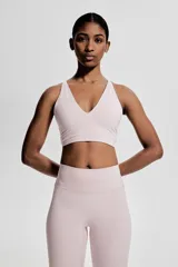 Top deportivo color rosa claro, de sujeción suave, confeccionado en tejido funcional con tecnología SoftMove™ y DryMove™. Tiene breteles finos cruzados en la espalda y copas forradas con relleno extraíble.