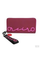 Billetera tipo tarjetero con cierre de cremallera, color fucsia/magenta, con el nombre "Oreiro" estampado en cursiva en color rosa neón en el frente. Incluye un llavero de muñequera de tela negra con la palabra "Oreiro" en rosa neón y un dije circular rojo con forma de labios.