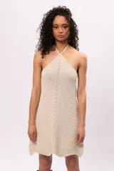 Vestido corto color crema, tejido en punto con diseño de líneas horizontales y diagonales. Escote halter con tiras finas.