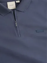 Chomba azul de manga larga con cuello polo y cierre de cremallera parcial. Tiene un pequeño logo de la marca en el pecho. Confeccionada en algodón orgánico.