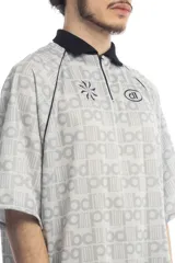 Remera deportiva blanca con cuello polo negro, cierre parcial con cremallera, mangas cortas y estampado de letras grises.