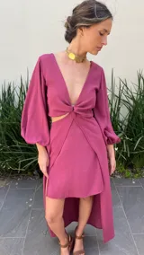 Vestido corto color fucsia, con escote en V, mangas largas abullonadas, abertura en la cintura y falda con volados.