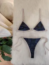 Conjunto de bikini negro con elástico tostado. El corpiño es de corte triangular con breteles regulables y aro metálico en el centro. La bombacha es tipo colaless con tiras laterales regulables.