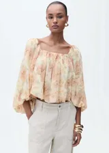 Blusa corta de gasa color crema con estampado floral en tonos durazno y verde. Tiene escote cuadrado, mangas largas abullonadas y espalda abierta.