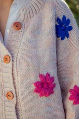 Cardigan tejido en lana color rosa claro con flores bordadas a mano en colores fucsia y azul. Tiene cuello redondo, cierre frontal con botones de madera y mangas largas.