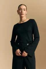 Top negro de manga larga acampanada con escote pronunciado en la espalda que se ajusta con lazos. La tela presenta una textura sutil con brillo, similar a un animal print discreto.