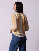 Blusa de gasa estampada a rayas verticales en tonos celeste, lila, naranja y marrón. Tiene cuello a la base con escote en V y botones. Delantera con bolsillo aplicado. Largo de manga regulable con presilla y botón. Terminación anudada opcional.