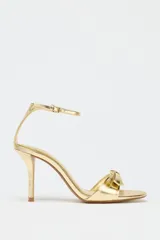 Sandalias doradas de tacón fino con tira delantera con detalle de lazo y tira con hebilla al tobillo.