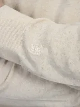 Sweater de punto color beige claro, de corte clásico y cuello redondo.