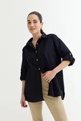 Camisa blanca de corte amplio, con cuello clásico, cierre frontal con botones y mangas largas con puños abotonados.