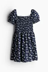 Vestido corto de popelina azul marino con estampado de pequeñas flores blancas, escote cuadrado con elástico fino sobre los hombros, mangas cortas abullonadas con fruncido elástico, cuerpo ajustado fruncido y falda con vuelo. Ribete de volado en escote y puños.