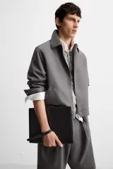 Bolso tipo sobre negro de cuero, con costura central y asa de mano. Cierre con cremallera y compartimentos interiores.