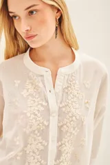 Camisa blanca de voile con rayas finas, corte amplio, cartera con botones y bordado de flores en el frente.