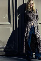 Vestido largo tipo camisero con estampado de cuadros en tonos marrón, negro y blanco. Tiene cuello solapa, mangas largas con puños abotonados, dos bolsillos de parche con solapa en el pecho y cierre frontal con botones a presión.