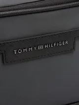 Riñonera negra de poliéster con acabado liso y logo metálico de Tommy Hilfiger en el frente. Cuenta con cierre de cremallera, cartera ajustable, compartimento principal y bolsillo exterior con cremallera.