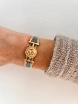 Pulsera con banda de terciopelo gris y apliques dorados con forma de moneda antigua.