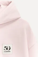 Sudadera rosa pálido con capucha, cierre frontal con cremallera, bolsillos tipo canguro y logo bordado en el pecho.