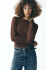 Sweater negro de punto liso con cuello redondo y mangas largas con botones dorados en los puños.