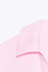 Camisa celeste de popelín con cuello solapa, escote pico y manga corta. Presenta dos bolsillos delanteros de parche y cierre frontal con botones.