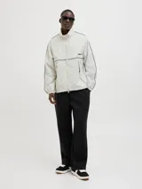 Campera deportiva color crema, de corte recto y cuello alto. Presenta cierre frontal, bolsillos laterales y mangas largas con puños elásticos. Detalle de líneas negras en hombros y mangas, y logo estampado en el pecho.