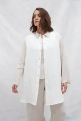 Camisa larga de lino color beige, con cuello camisero y cierre frontal con botones. Tiene mangas largas con puños abotonados, bolsillos laterales y una franja a contratono en la espalda y mangas.