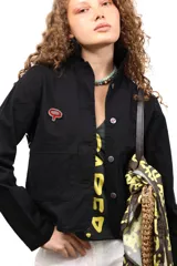 Chaqueta marrón de algodón con botones metálicos, cuello clásico, bolsillos frontales y apliques de tachas y botones formando una flor en la espalda.