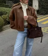 Chaqueta tipo bomber de gamuza color marrón, con cuello camisero, calce suelto y mangas amplias.