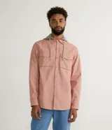 Camisa overshirt color salmón de sarga de algodón con capucha gris ajustable con cordones. Tiene cierre frontal con botones, dos bolsillos con solapa en el pecho y mangas largas con puños abotonados.
