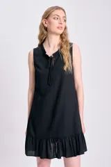 Vestido corto negro sin mangas, confeccionado en lino, con escote redondo con lazo y volados en el ruedo.