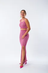 Conjunto tejido de color fucsia brillante, compuesto por un top corto con tirantes finos y una falda larga con abertura lateral.