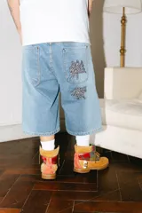 Bermuda baggy de jean celeste con lavado gastado en los laterales y bordados de letras chinas en negro y blanco.