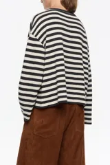 Camiseta de tejido de punto de manga larga, con patrón de rayas horizontales anchas en blanco crudo y negro. Presenta cuello redondo con ribete negro y un pequeño bordado amarillo en el pecho.