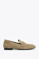 Zapato mocasín color beige de serraje con detalle de tira en la parte delantera y acabado en punta redonda.