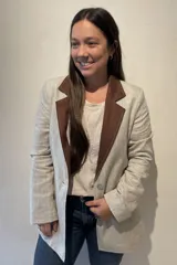 Blazer de lino color beige con solapas y cuello en marrón. Corte entallado, con botón de nácar, tajo atrás y bolsillos a los costados.