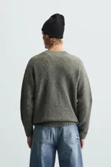 Sweater verde oliva de punto con cuello redondo, manga larga y diseño de trenzas en el frente.