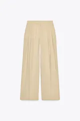 Pantalón color beige de lino, de tiro alto, con pinzas delanteras, bolsillos frontales y pernera ancha.